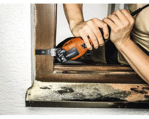Handwerker verwendet ein elektrisches Multifunktionswerkzeug mit Starlock Max Aufnahme zum Schneiden an einem Holzfensterrahmen.