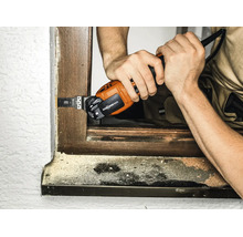Person verwendet ein Multifunktionswerkzeug mit Starlock Max Aufnahme zum Schneiden eines Holzrahmens an einem Fenster