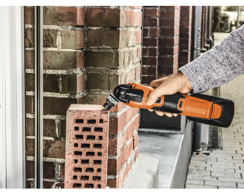 Eine Hand hält ein Akku Multitool Starlock Plus, das zum Bearbeiten eines Ziegelsteins verwendet wird.