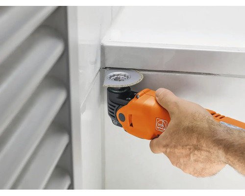 Ein Fein Multitool mit einem segmentierten Diamantsägeblatt schneidet eine Fliesenfuge an einer Wand.