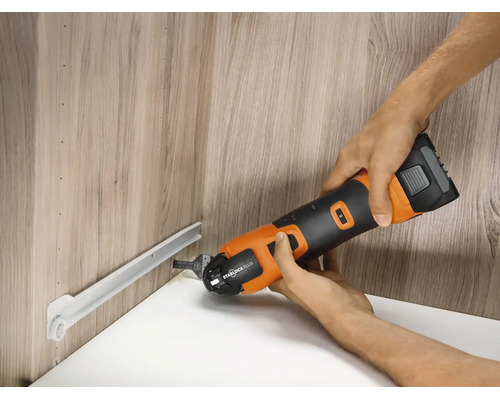 Eine Person benutzt ein oszillierendes Multifunktionswerkzeug mit Starlock Plus Aufnahme zum Schneiden einer Metallschiene in einem Holzschrank.