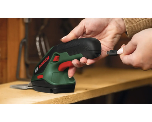Person hält eine Bosch Akku Gras- und Strauchschere und bereitet das Aufladen per USB Kabel vor.