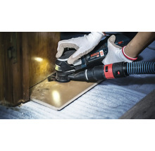 Ein Bosch Professional Akku Multischneider beim Schneiden eines Holzteils mit angeschlossener Staubabsaugung.