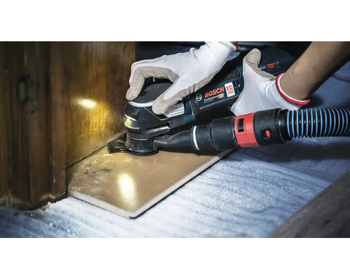 Ein Bosch Professional Akku Multischneider beim Schneiden eines Holzteils mit angeschlossener Staubabsaugung.