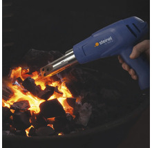Eine Hand hält eine Steinel HL 1620 S Heißluftpistole mit Grillanzünder Aufsatz über glühender Grillkohle.