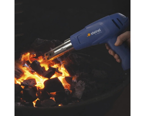Eine Hand hält eine Steinel HL 1620 S Heißluftpistole mit Grillanzünder Aufsatz über glühender Grillkohle.