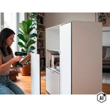 Eine Frau montiert einen Schrank mit einem Akku-Schrauber in einem hellen Wohnzimmer. (Image AI modified or generated)