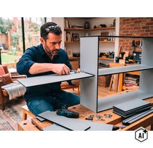 Ein Mann baut in einer Werkstatt ein Regal aus Holzplatten zusammen und nutzt dazu einen Schraubendreher und einen Akkubohrschrauber. (Image AI modified or generated)