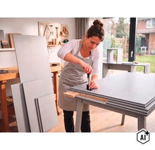 Eine Frau montiert in einer hellen Werkstatt Möbelbauteile aus Holz mit einem Schraubendreher an einem Werktisch. (Image AI modified or generated)