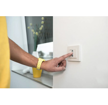 Person betätigt einen weißen Wandschalter an einer Wand.