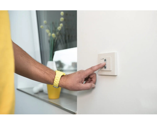 Person betätigt einen weißen Wandschalter an einer Wand.