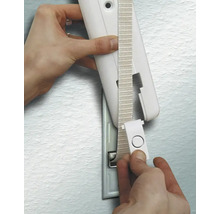 Eine Hand führt das Gurtband eines Rollladengurts durch die Abdeckung eines Gurtwicklers an einer Wand.
