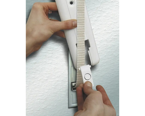 Eine Hand führt das Gurtband eines Rollladengurts durch die Abdeckung eines Gurtwicklers an einer Wand.