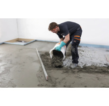 Handwerker gießt Estrichmörtel aus einem Eimer auf einen Boden in einem leeren Raum.