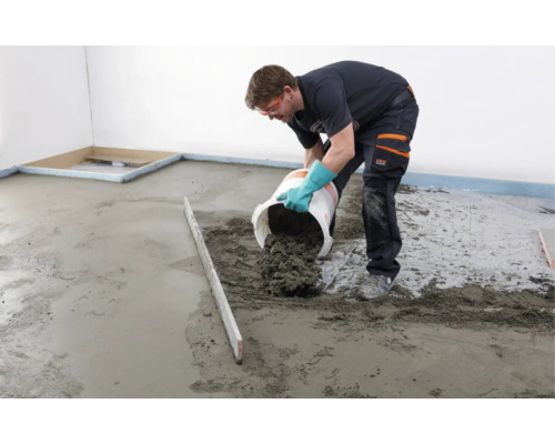 Handwerker gießt Estrichmörtel aus einem Eimer auf einen Boden in einem leeren Raum.