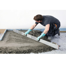Handwerker zieht mit einer Abziehlatte frischen Estrich glatt auf einem Boden.