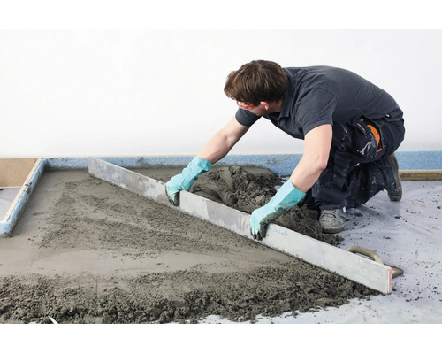 Handwerker zieht mit einer Abziehlatte frischen Estrich glatt auf einem Boden.