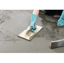 Handwerker glättet mit einer Reibebrett Kelle einen frischen Estrich auf einer Bodenfläche