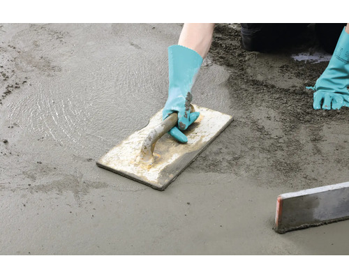 Handwerker glättet mit einer Reibebrett Kelle einen frischen Estrich auf einer Bodenfläche