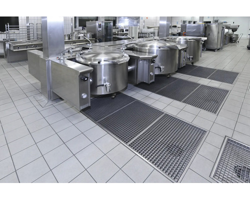 Professionelle Großküche mit Edelstahlkochkesseln und Bodenabläufen in einer industriellen Arbeitsumgebung