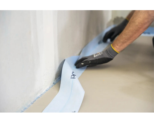 Handwerker beim Anbringen eines Randdämmstreifens an einer Wand entlang des Bodens für eine fachgerechte Estrichverlegung.