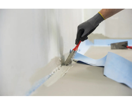 Hand eines Arbeiters in Schutzhandschuhen verarbeitet Dichtschlämme mit einem Pinsel an einem Wand Boden Übergang mit einem Dichtband