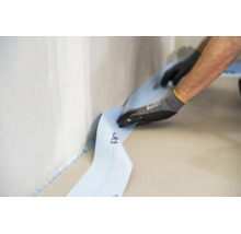 Handwerker beim Anbringen eines Randdämmstreifens an einer Wand entlang des Bodens für eine fachgerechte Estrichverlegung.