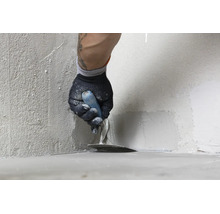 Handwerker beim Auftragen von Dichtschlämme oder Spachtelmasse in der Wandecke mit einer Glättkelle