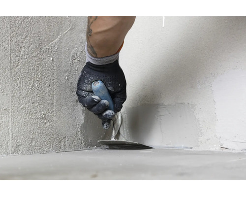 Handwerker beim Auftragen von Dichtschlämme oder Spachtelmasse in der Wandecke mit einer Glättkelle