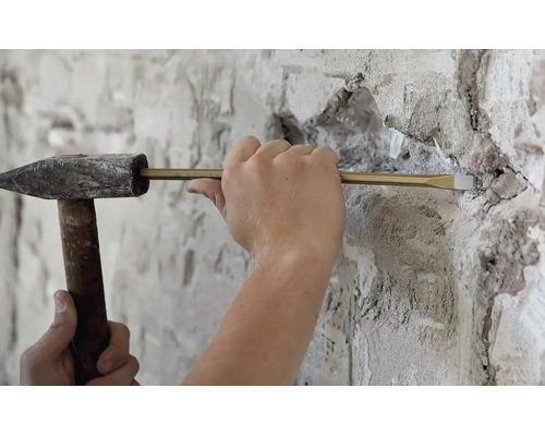 Handwerker bei der Arbeit mit einem Schlosserhammer und einem Meißel zum Abtragen von Mauerwerk an einer verputzten Wand.