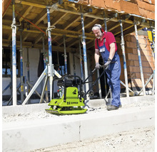 Handwerker bedient eine Zipper Rüttelplatte auf einer Baustelle mit Schalungsstützen.