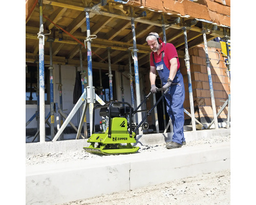 Handwerker bedient eine Zipper Rüttelplatte auf einer Baustelle mit Schalungsstützen.
