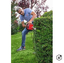 Mann schneidet mit einer elektrischen Heckenschere eine Gartenhecke in einem privaten Garten (Image AI modified or generated)