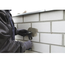 Handwerker beim Ausbessern einer Fuge an einer Mauer aus hellen Steinen mit einer Fugenkelle.