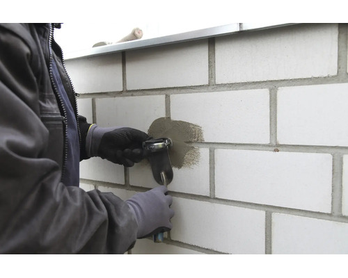 Handwerker beim Ausbessern einer Fuge an einer Mauer aus hellen Steinen mit einer Fugenkelle.
