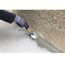 Handwerker zieht mit einer Maurerkelle einen Hohlkehlenmörtel zwischen Boden und rauer Betonwand