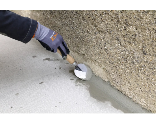 Handwerker zieht mit einer Maurerkelle einen Hohlkehlenmörtel zwischen Boden und rauer Betonwand