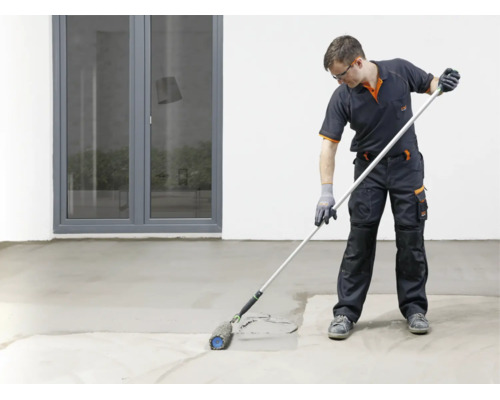 Handwerker in Arbeitskleidung bei der Arbeit mit einer Stachelwalze zum Entlüften von Estrich oder Ausgleichsmasse auf einem Boden.