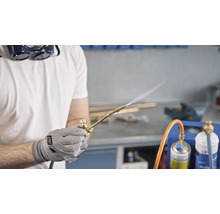 Handwerker mit Schutzbrille verwendet einen Gaslötbrenner in einer Werkstatt.