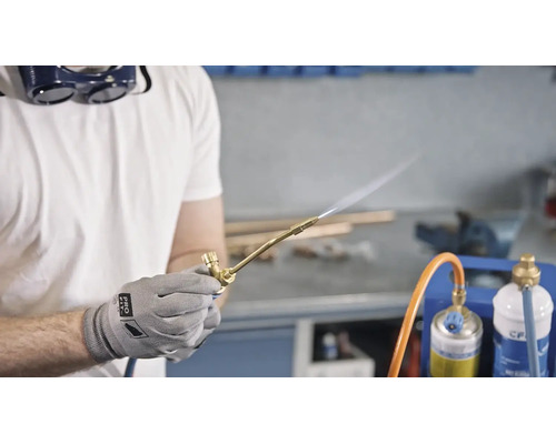 Handwerker mit Schutzbrille verwendet einen Gaslötbrenner in einer Werkstatt.