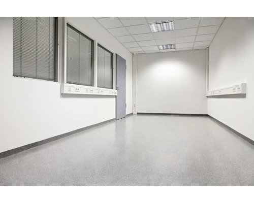 Leeres, funktionales Büro oder Gewerberaum mit weißen Wänden, grauem Bodenbelag, Rasterdecke und Fensterfronten mit Jalousien.