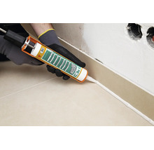 Handwerker mit Kartuschenpresse beim Auftragen von PCI Silcoferm S Silikon an der Sockelleiste einer Fliesenwand