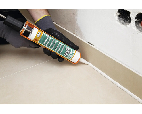 Handwerker mit Kartuschenpresse beim Auftragen von PCI Silcoferm S Silikon an der Sockelleiste einer Fliesenwand
