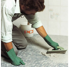 Handwerker beim Verfugen eines Mosaikfliesenbodens mit einem Glättbrett und PCI Eimer im Hintergrund.