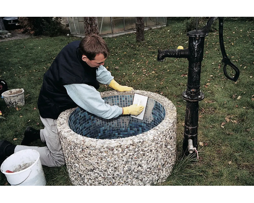 Handwerker beim Verfugen eines runden Gartenbrunnens mit Mosaikfliesen im Außenbereich.