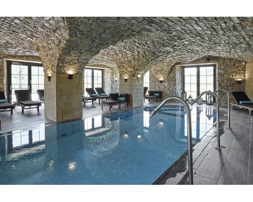 Innenpool in einem Gewölbekeller mit Natursteinwänden und Liegestühlen in einem Wellnessbereich.