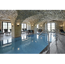 Innenpool in einem Gewölbekeller mit Natursteinwänden und Liegestühlen in einem Wellnessbereich.