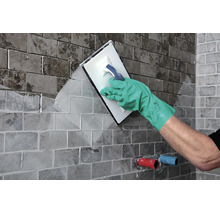 Handwerker beim Verfugen von Fliesen an einer Wand mit einem Fugbrett und Schutzhandschuhen