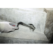 Hand in Arbeitshandschuh spachtelt Mörtel mit einer Maurerkelle in ein Loch in einer Betonwand.