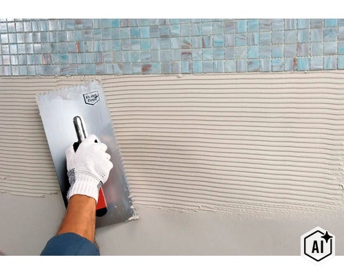 Eine Hand in einem Handschuh trägt mit einer Zahnkelle Fliesenkleber auf eine Wand unterhalb von Mosaikfliesen auf. (Image AI modified or generated)